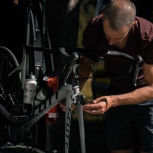 Cyclist working on adjusting the front fork of a Scott road bike mounted on a repair stand, with a van in the background.