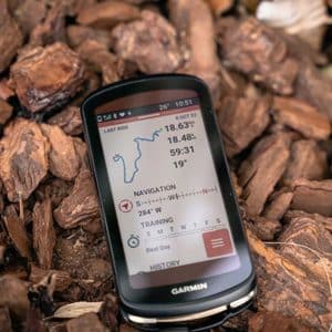 Close-up of a Garmin cycling computer displaying ride stats and navigation, placed on a bed of bark mulch.