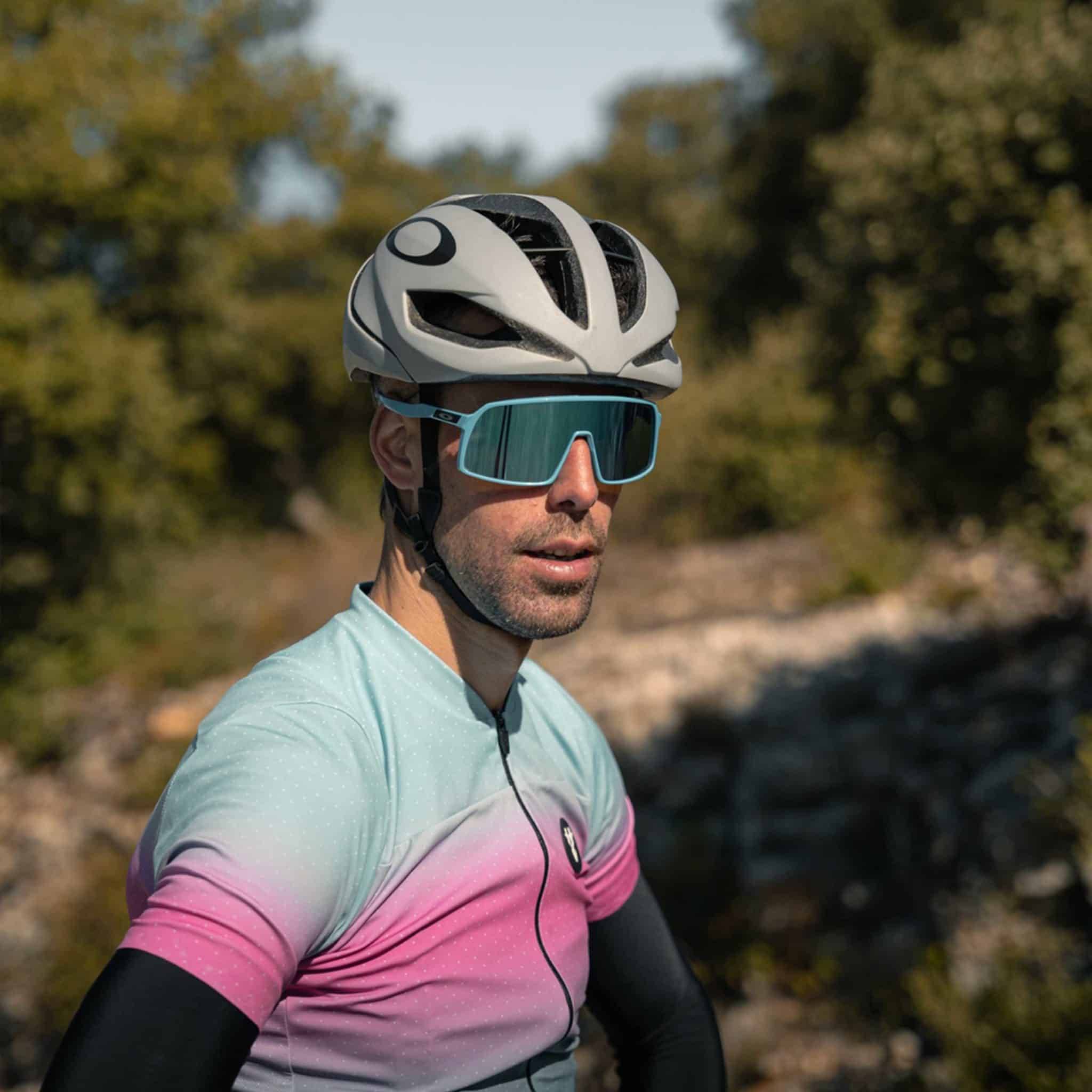 Close-up of a cyclist wearing a gradient pink and blue jersey, modern helmet and oversized cycling sunglasses.