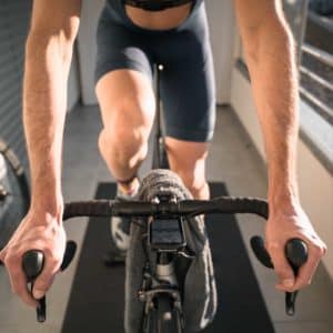 Cyclist training indoors on a stationary bike, with close focus on handlebars, bike computer and cyclist's hands.