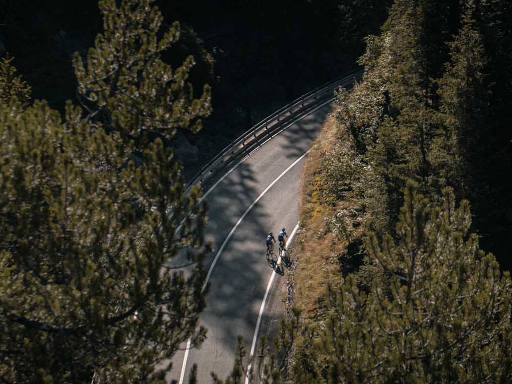 Two cyclists riding through a winding forest road, showcasing the tranquility and beauty of a road cycling tour in nature.