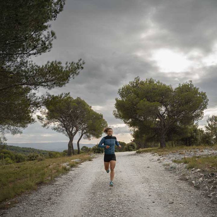 Trail runner on a gravel path surrounded by pine trees under a cloudy sky.