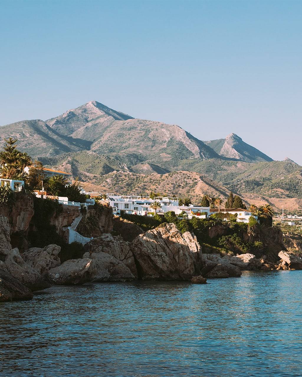 A picturesque coastal village with rugged cliffs and towering mountains in the background, providing the perfect setting for a triathlon training camp with scenic swim, bike, and run opportunities.