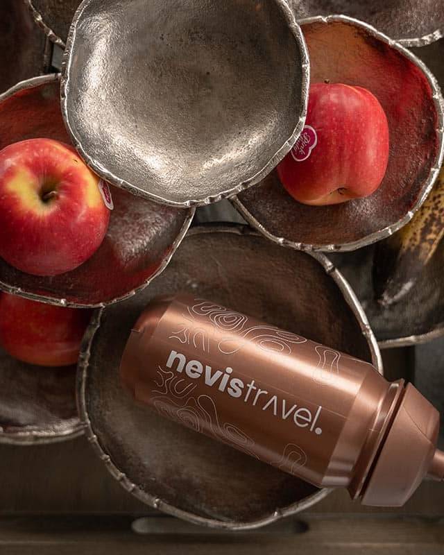 A nevistravel. branded water bottle placed alongside fresh apples and bananas in rustic bowls, highlighting essential snacks and hydration for cycling holidays.