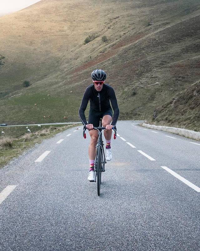 A cyclist climbing a quiet mountain road surrounded by rolling hills and grazing sheep, showcasing the challenges and beauty of cycling holidays in the countryside.