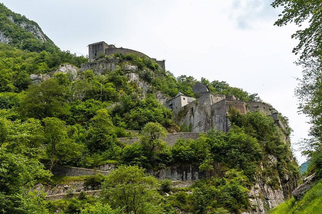 Historical fortress perched on a lush green hill along a winding road in the French Pyrenees.