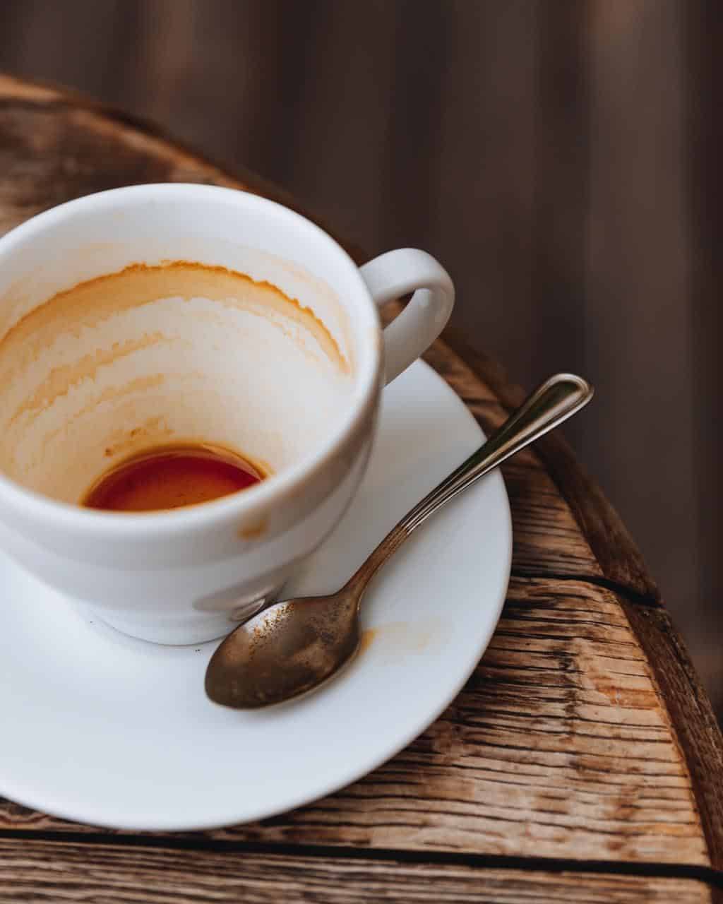 Empty hot coffee in white ceramic cup with dirty spoon after drink on wooden table with copy space. Aftertaste of aroma cappuccino in coffee shop