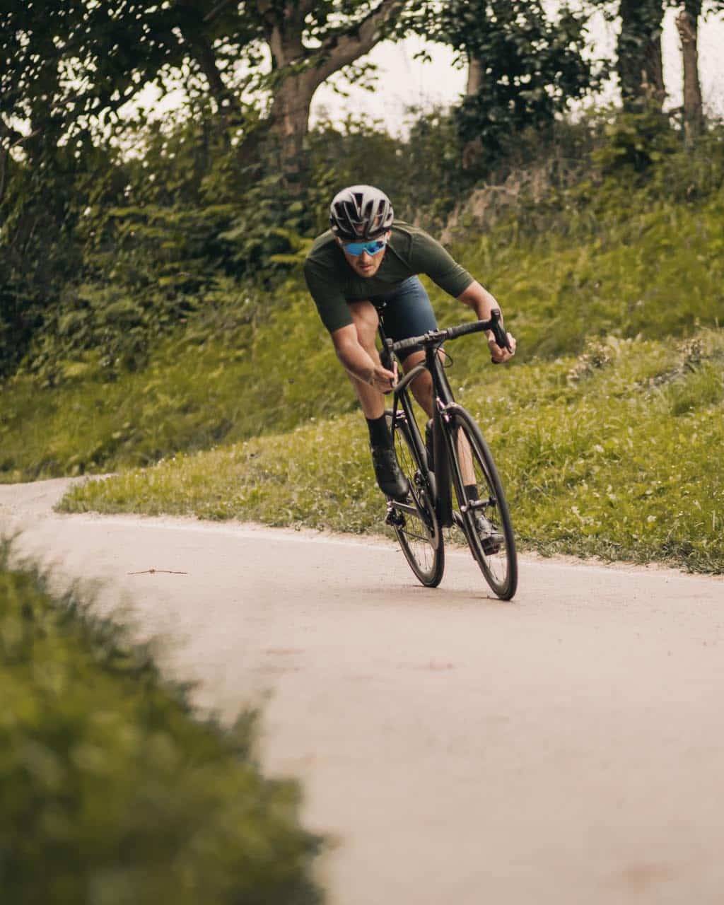 Young man with muscular legs wearing safety helmet and glasses racing alone at green city park. Professional cyclist training regularly on fresh air.