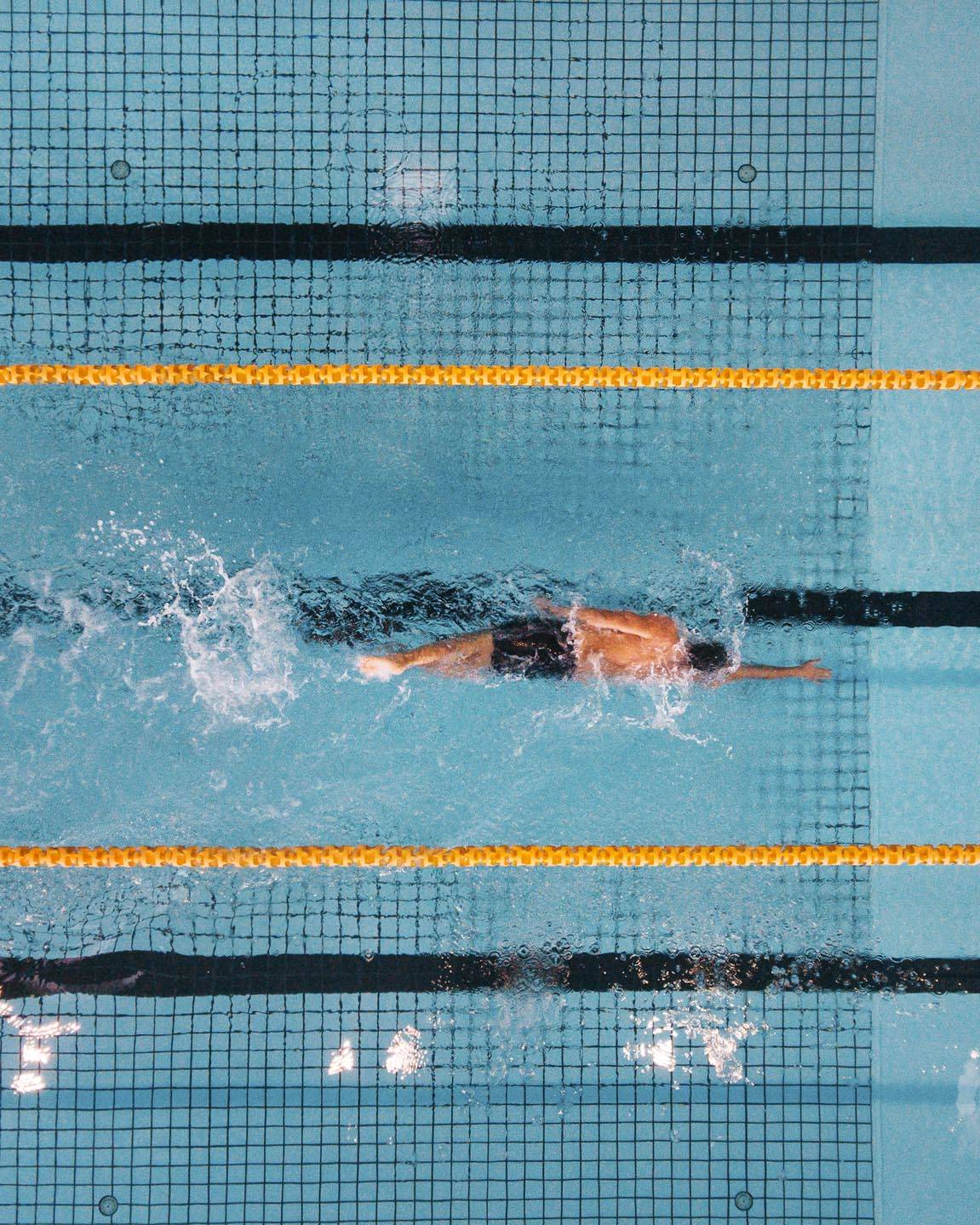 Top view shot of young man swimming laps in a swimming pool. Male swimmer swimming the front crawl in a pool.