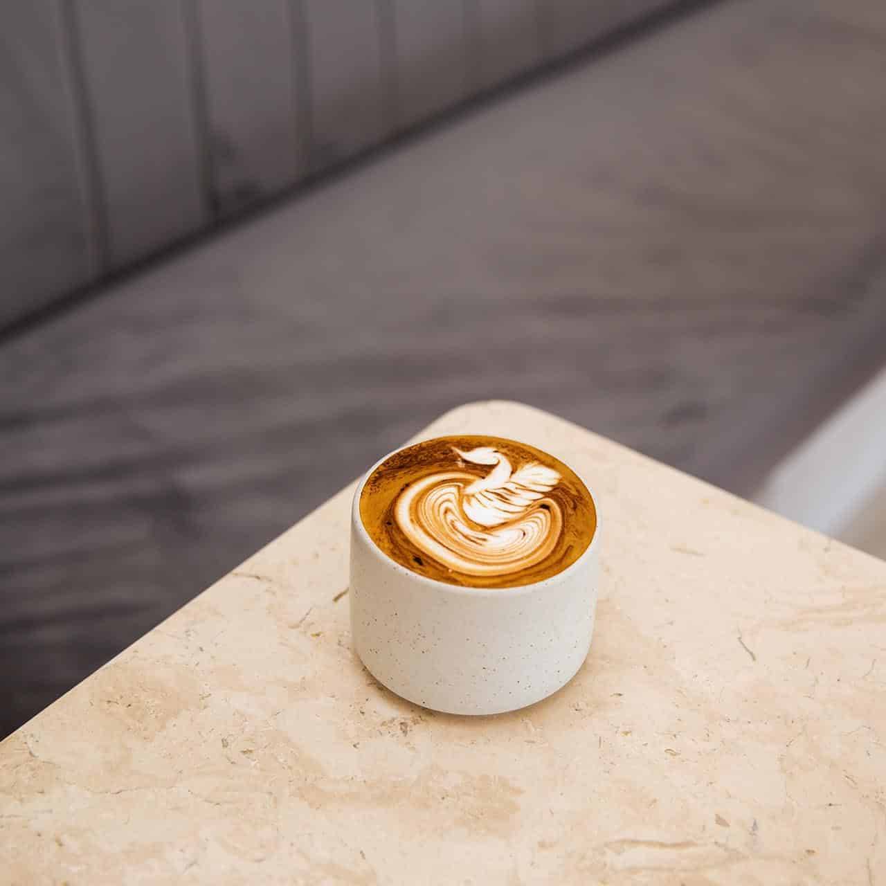 A beautifully crafted artisan latte with intricate foam art served in a ceramic cup on a marble table, capturing the essence of contemporary café culture.