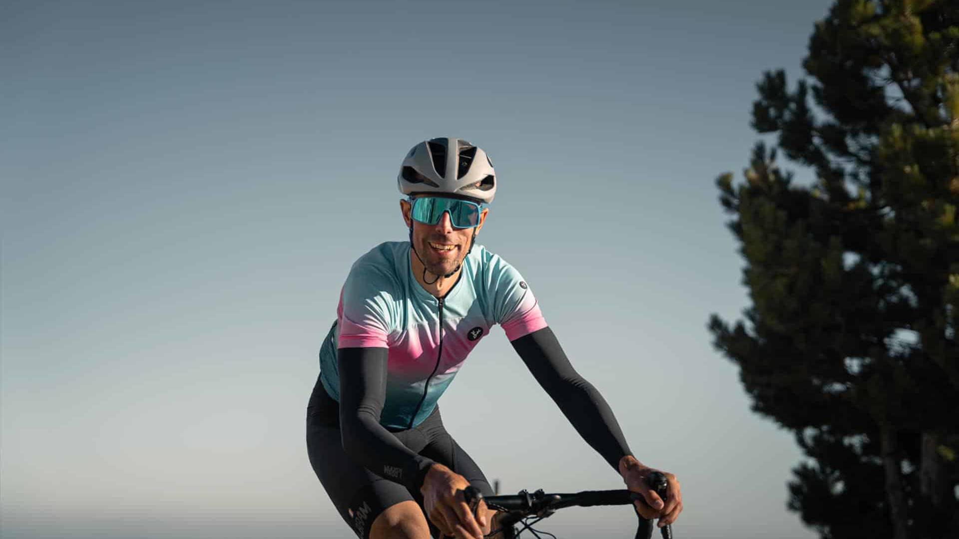 Cyclist smiling during a ride on a clear day with scenic views in the background.