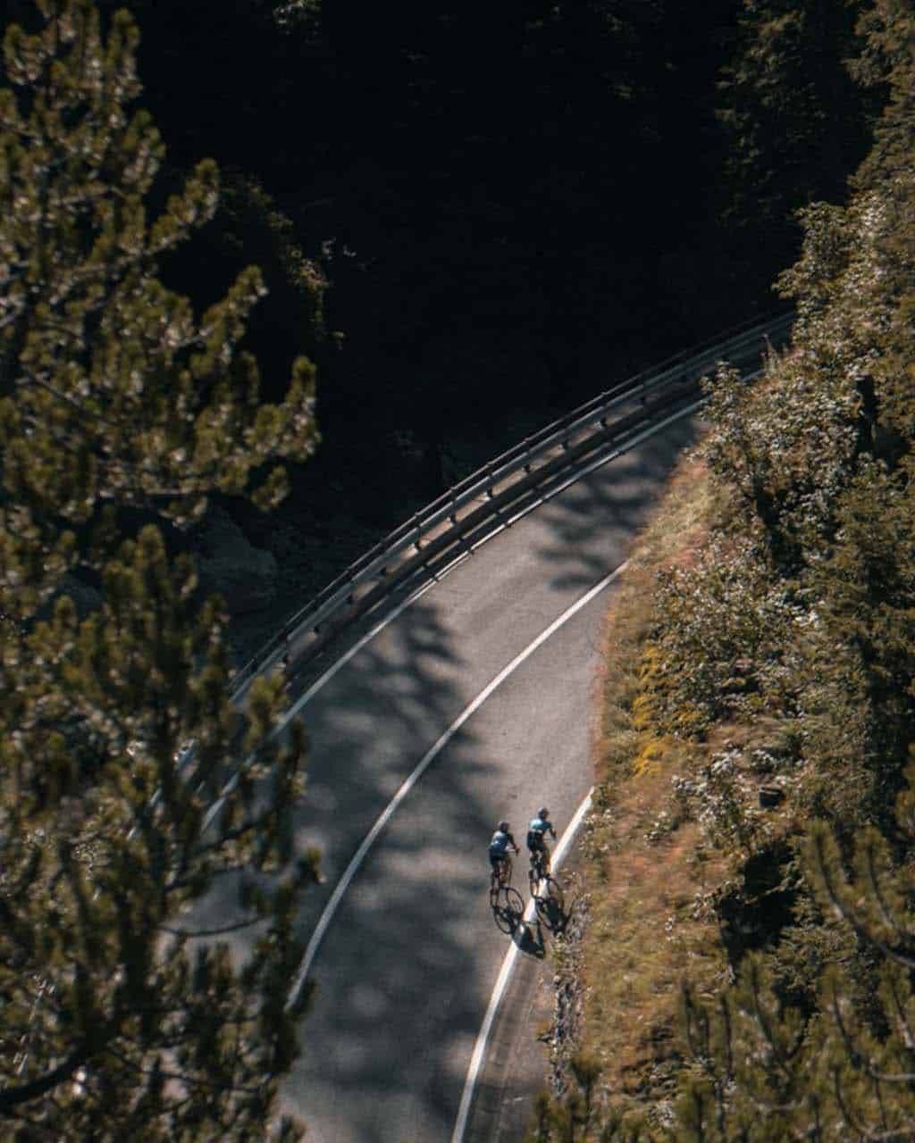 Two cyclists riding through a winding forest road, showcasing the tranquility and beauty of a road cycling tour in nature.