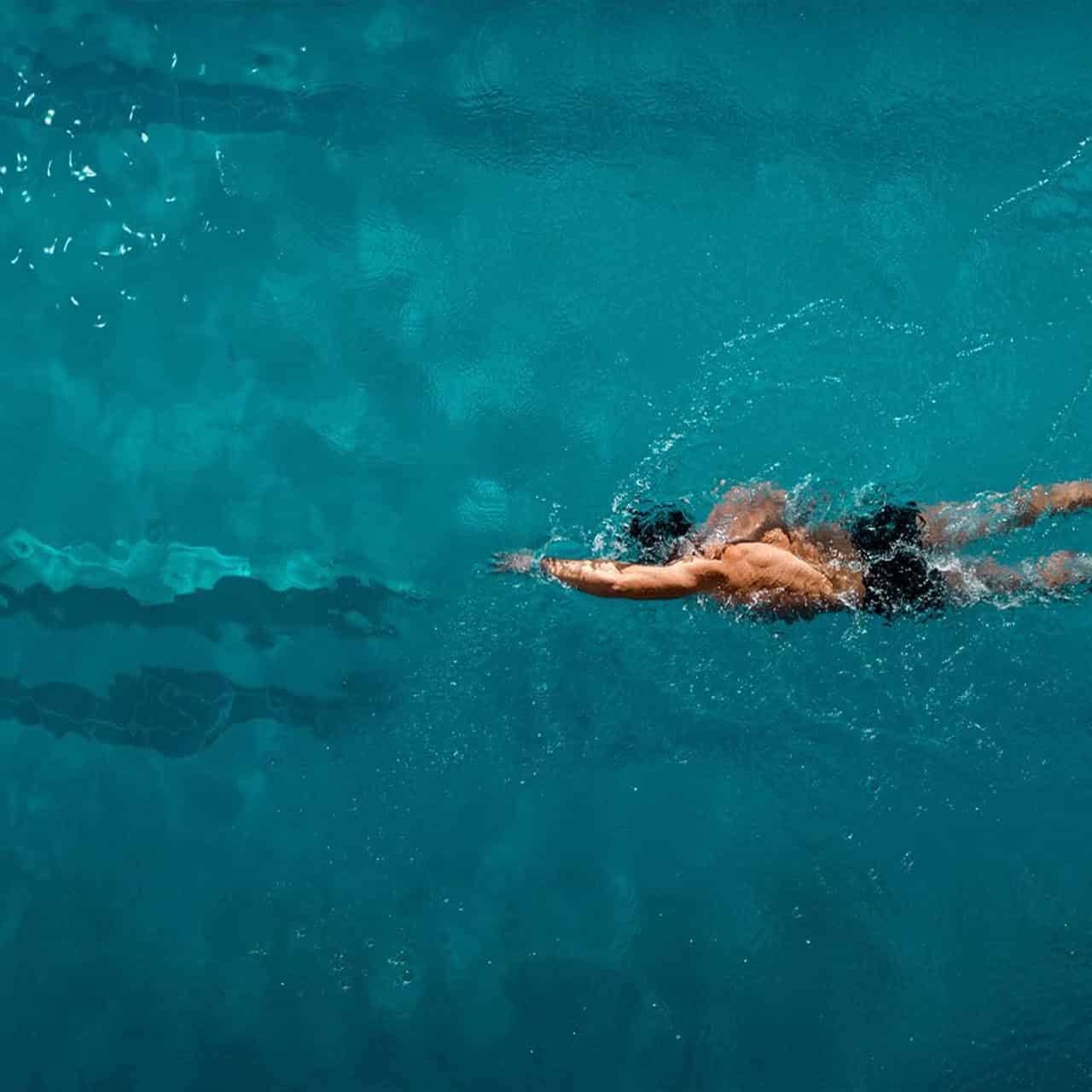 A swimmer performing freestyle strokes in a crystal-clear swimming pool during a training session.