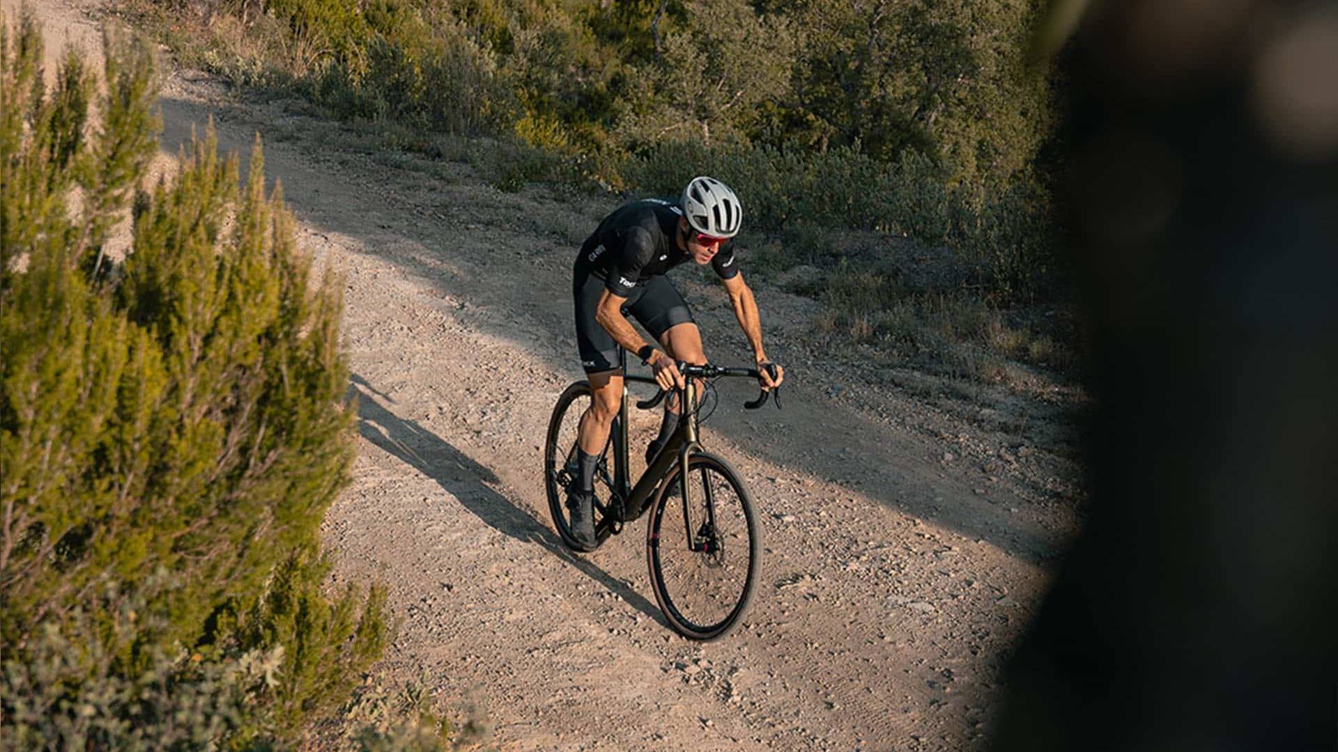 Cyclist climbing a rugged trail surrounded by Mediterranean shrubland and scenic hills, showcasing the thrill of gravel biking.