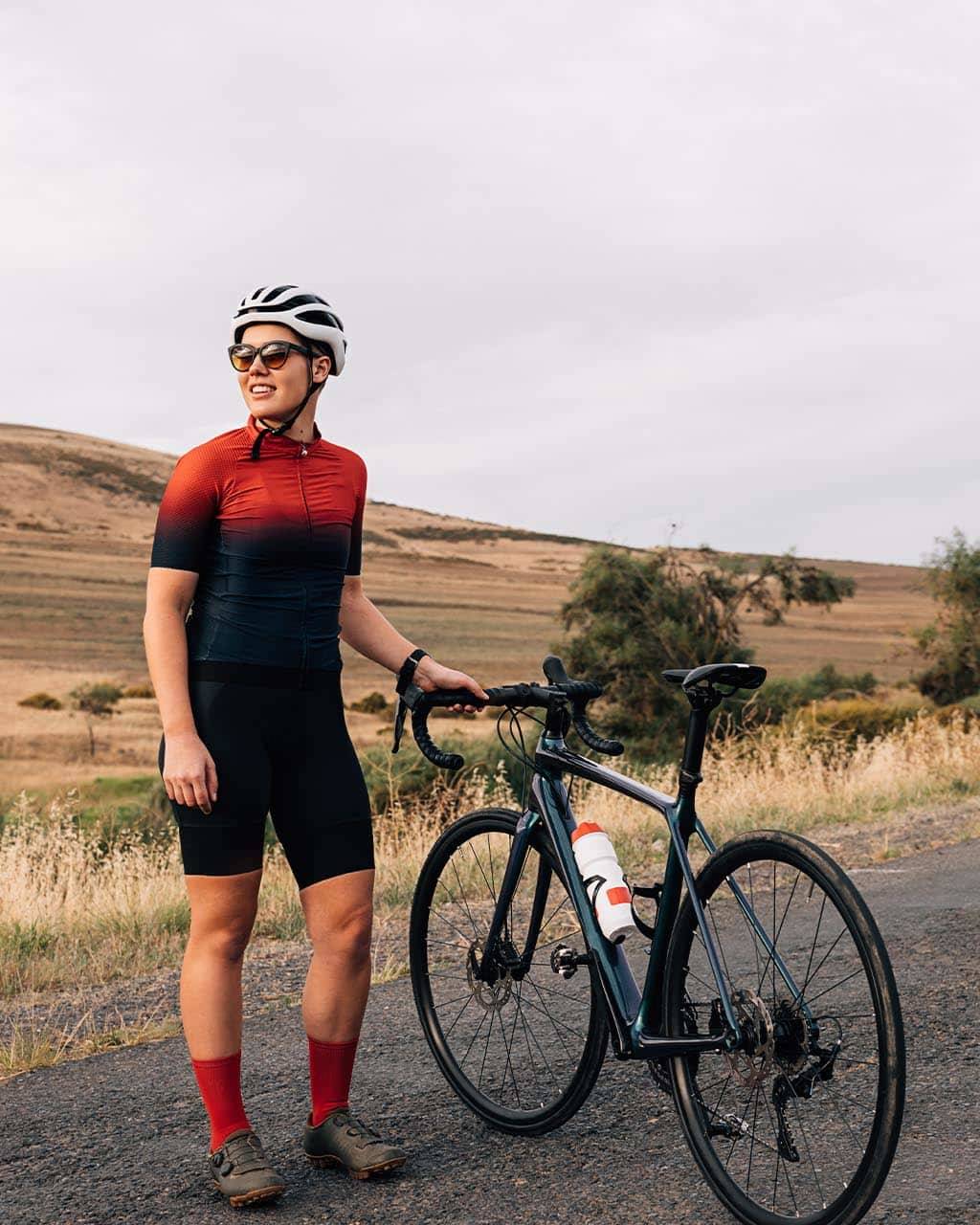 A cyclist in a red jersey standing beside their bike on a quiet country road, illustrating how to plan a cycling holiday for scenic adventures and peaceful exploration.