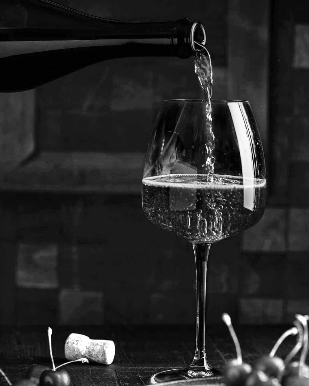 A close-up shot of red wine being poured into a glass outdoors with a blurred background