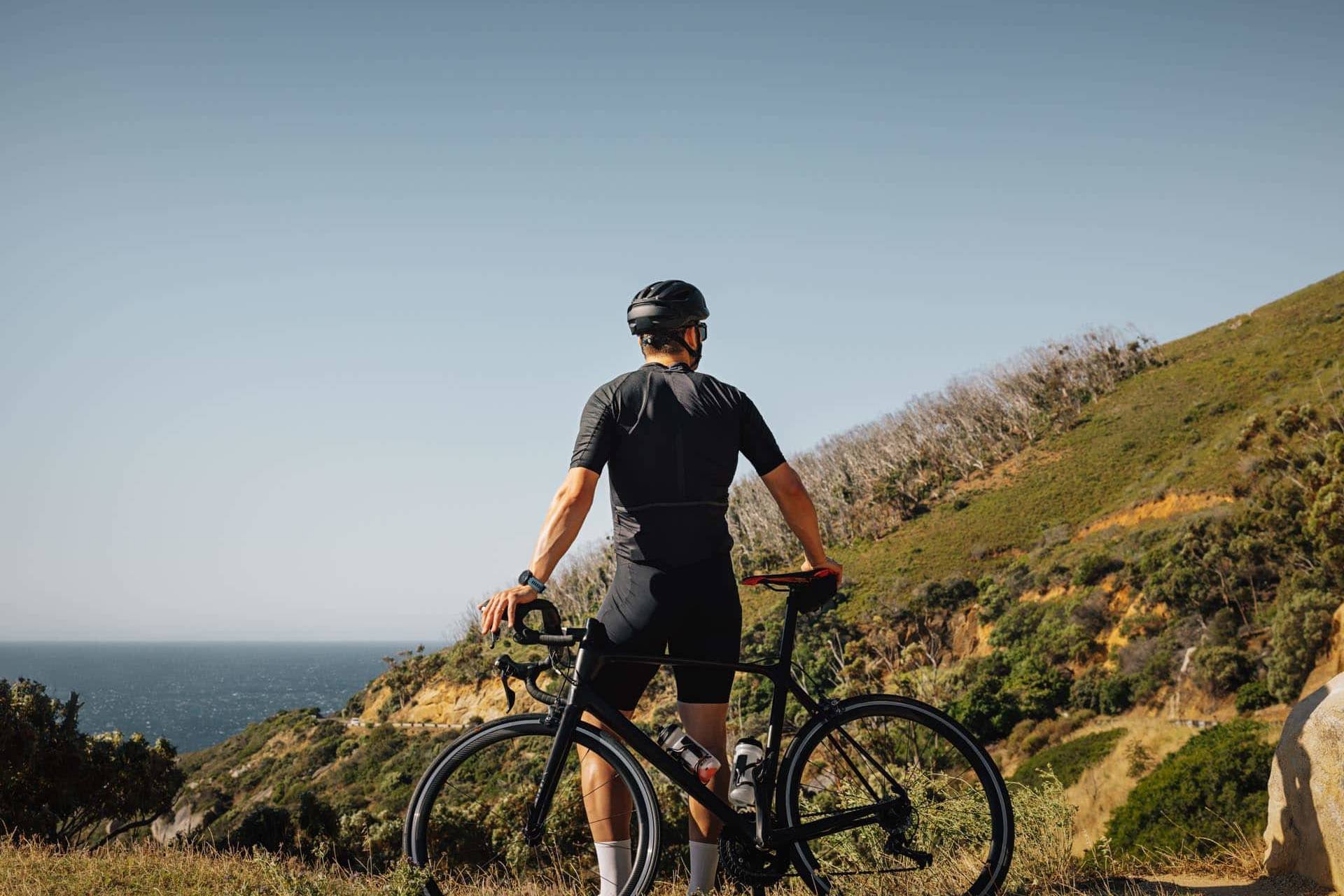 Back view of a male cyclist leaning on his road bike relaxing during training, enjoying the view