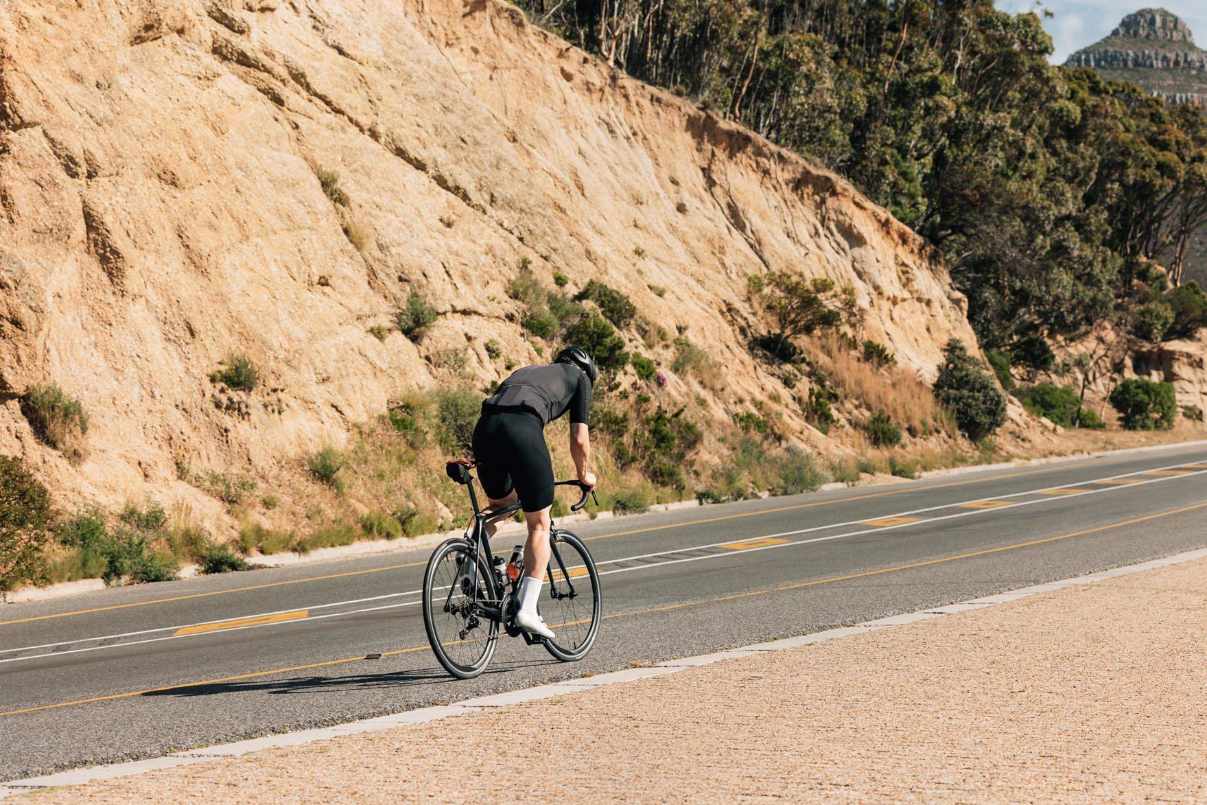 Rear view of a professional cyclist riding up on an empty road. Young male in cycling attire on a road bike.